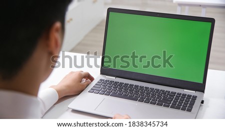 back view of asian businessman look at green screen laptop in office
