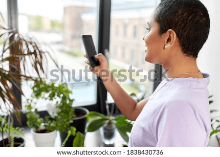 technology and people concept - smiling african american woman with smartphone and indoor plants at home