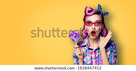 Purple head excited very surprised woman with lollipop. Pinup girl in rose pink red glasses with wide opened mouth, eyes. Retro and vintage concept. Yellow orange color background with text copy space