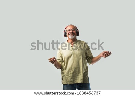 happy senior Indian asian bearded man smiling using headphones with smartphone or tablet against white background, presenting screen or dancing Royalty-Free Stock Photo #1838456737