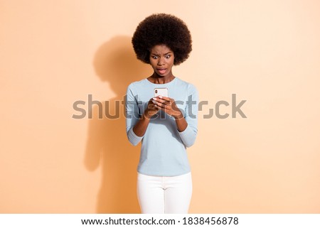 Photo portrait of shocked upset curly dark skinned girl using smartphone reading message in social media isolated on beige color background