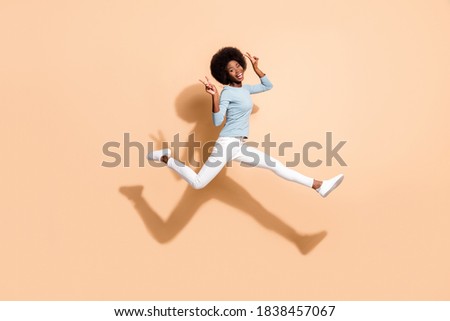 Photo portrait of african american girl holding two v-signs flying in air isolated on pastel beige colored background