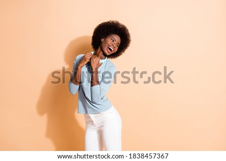 Photo portrait of black skinned girl holding cyan wireless headphones laughing isolated on pastel beige colored background