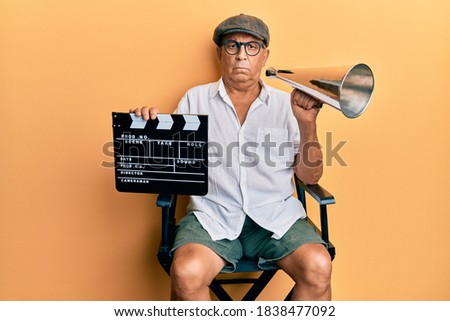 Handsome mature director man holding video film clapboard and louder skeptic and nervous, frowning upset because of problem. negative person.  Royalty-Free Stock Photo #1838477092