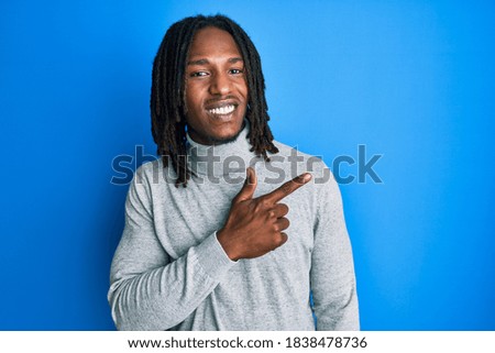 African american man with braids wearing turtleneck sweater cheerful with a smile of face pointing with hand and finger up to the side with happy and natural expression on face 
