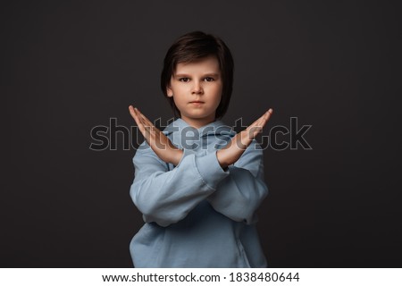 Image of serious boy 10-12 years old, dressed in casual clothes making X sign with crossed hands, gesturing stop, warning of danger. No way, stop doing. Human emotions concept