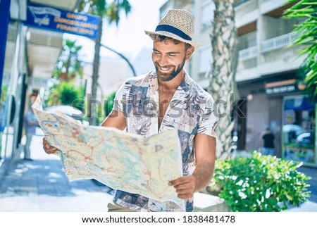 Young hispanic man on vacation smiling happy holding city map walking at street.