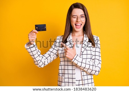 Photo portrait of young female worker pointing with finger at plastic card winking blinking isolated on vivid yellow color background