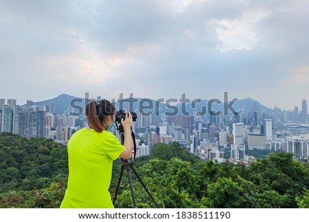Girl with face mask uses camera and tripod to takes photos of city Skyline of Hong Kong Island (south of Victoria Harbour) from Braemar hill in North Point during covid-19