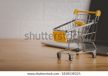 Shopping cart in with laptop on wood table in office background.Easy shopping with finger tips for consumers.concept of working at home through technology to shopping and sell things online.
