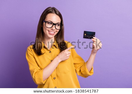 Photo of young pretty lady indicate finger look hold debit card wear spectacles yellow shirt isolated purple color background