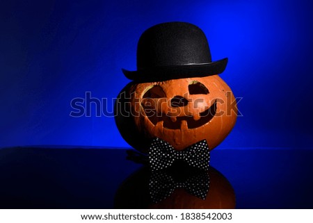 Pumpkin in a top black hat, with funny cut out face, isolated on a glowing blue background. Studio light. Space for writing on the left. Halloween card.