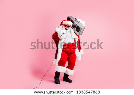 Full length photo cool crazy grey white hair beard santa claus big belly sing x-mas christmas eve noel song hold boom box mic wear suspenders cap sunglass isolated pink color background