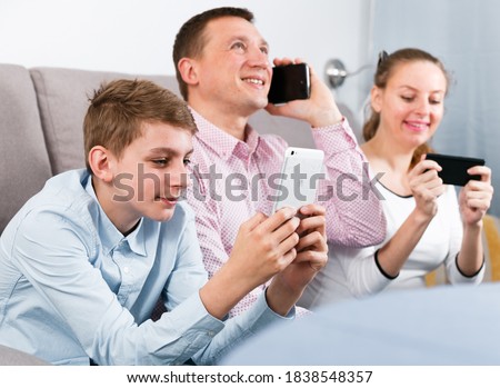 Middle-aged happy family playing with their smartphones together at home