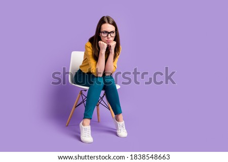 Full length photo of lady sit chair arms chin look empty space wear yellow shirt blue pants specs sneakers isolated purple color background Royalty-Free Stock Photo #1838548663