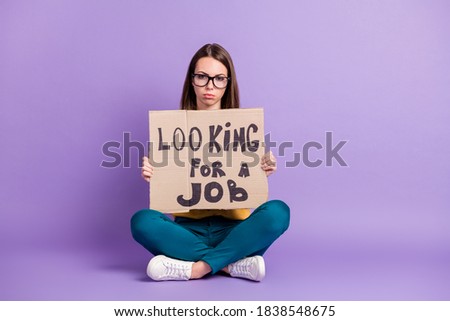Photo portrait of depressed sitting down girl wearing glasses keeping placard of job searching isolated on bright purple color background