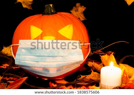 Jack o lantern on adark and yellow maple leaves background with dry leaves, candle and medical face mask.