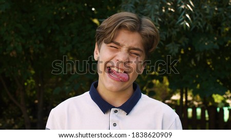 Close-up of the face of a young, cute, Caucasian boy who is making faces at the camera, making different grimaces with his facial expressions. Positive emotion. On the street. Royalty-Free Stock Photo #1838620909