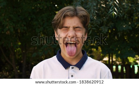 Close-up of the face of a young, cute, Caucasian boy who closes his eyes and shows his tongue to the camera. Positive emotion. On the street. Royalty-Free Stock Photo #1838620912
