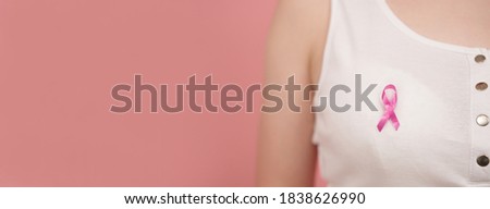 Symbol of breast cancer awareness month, pink october badge on the white shirt of unrecognizable woman. High quality photo