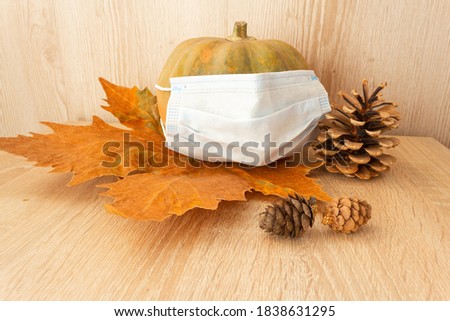 Pumpkin in a protective mask next to the cones on an autumn leaf and a wooden background. Autumn mood. Quarantine. Flu protection. Сovid