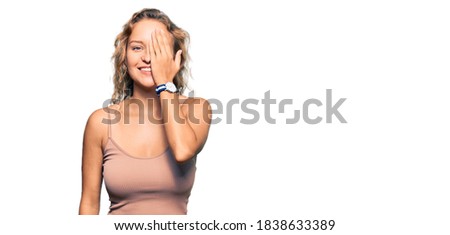 Beautiful caucasian woman wearing casual clothes covering one eye with hand, confident smile on face and surprise emotion. 