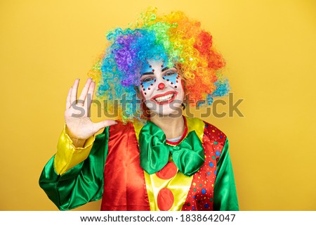 Clown standing over yellow insolated yellow background doing hand symbol