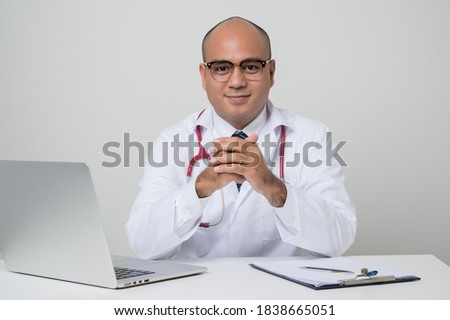 A portrait of Asian doctor put on stethoscope holding hand and smile sitting at the desk isolated on white background.