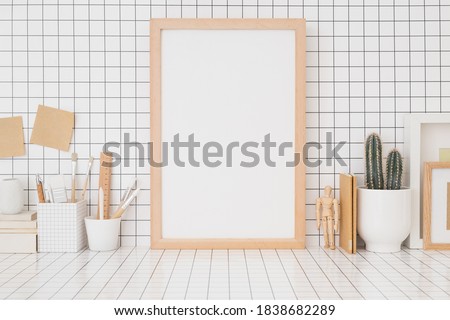 Wooden picture frame mockup on a checkered wall, wooden supplies, boxes, brushes on home office desk.