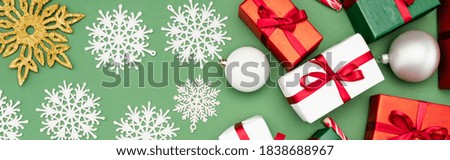 panoramic shot of colorful gift boxes, christmas balls and decorative snowflakes on green background, top view