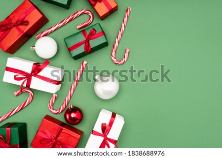 top view of multicolored gift boxes, candy canes and christmas balls on green background