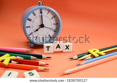 Block letters on tax with alarm clock and colorful pencils on orange background 