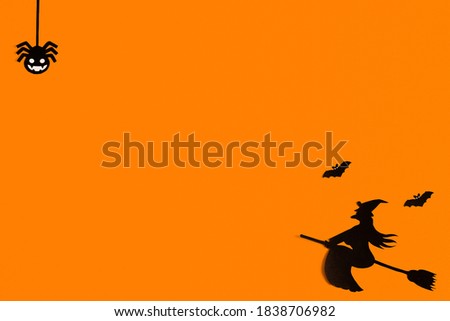 Silhouettes of a flock of bats and a witch flying on a broom made of black paper on an orange background. Halloween greeting template with copy space. Flat lay for your design. ready-made template
