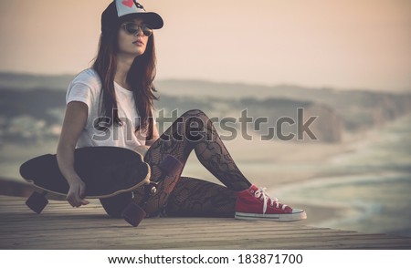 Beautiful fashion skater girl posing with  a skate board