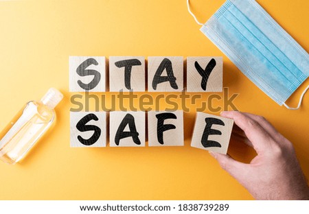 words STAY SAFE on wooden blocks on orange background with protective face mask and hand sanitizer