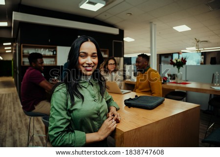 Portrait of Indian business woman smiling taking lunch break while colleagues prepare for meeting with partners 