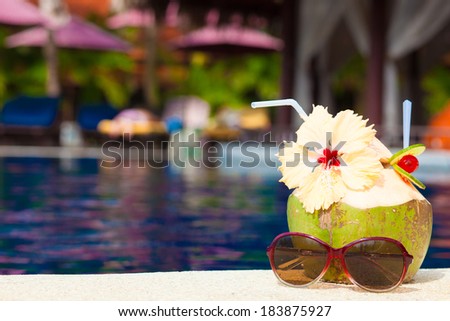 picture of fresh coconut cocktail and pink sunglasses near luxury pool