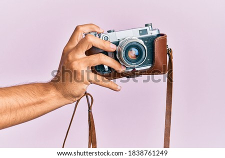Hand of young hispanic man holding vintage camera over isolated pink background.