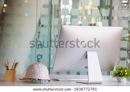 Close up view of engineer worktable with computer, safety helmet, stationery and copy space on white desk in glass partition office room.