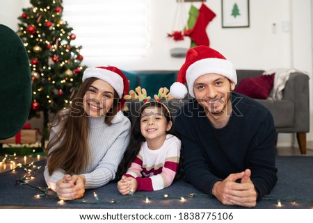 Portrait of a Hispanic family of three lying next to a Christmas tree at home and looking ready to celebrate