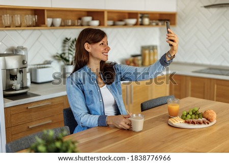 Beautiful woman taking picture of herself, at kitchen.