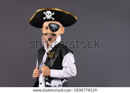 Little boy dressed as a pirate with makeup on his face is having fun at a Halloween party. Face painting for children. Isolated gray background with blank space.
