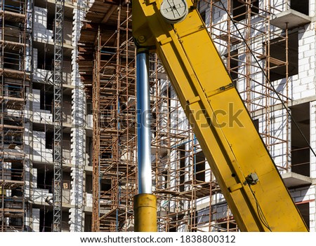 Part of a construction machine (excavator or crane) with multi-storey building under construction with scaffolding (new residential complex) on the background, Moscow, Russia