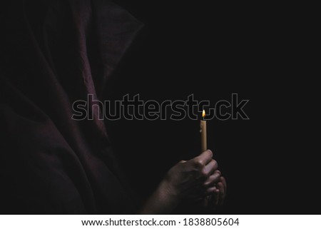 Young catholic nun is holding candle in her hands. Focus on candle. Face is blurred. Photo on black background.