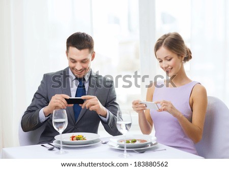 restaurant, couple, technology and holiday concept - smiling couple taking picture of appertizer with smartphone camera at restaurant