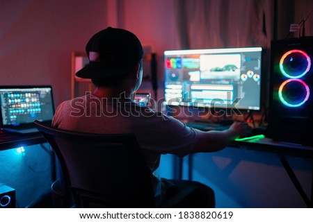 Blogger working editing video footage and looking at the monitor in-home office while working on post-production for a vlog. Selective focus person. Royalty-Free Stock Photo #1838820619