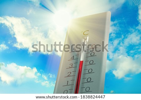 Weather thermometer showing high temperature and blue sky with clouds on background