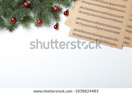 Music sheets near fir tree branches with Christmas balls and space for text on white background, flat lay
