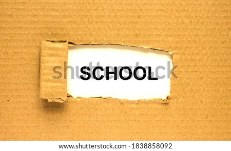 The word School appearing behind torn brown paper. Can be use as a concept photo