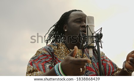 Afro-American in traditional african shirt is singing on microphone. High quality photo